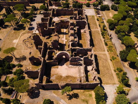 Aerial view of the ancient Roman ruins of the Baths of Caracalla, featuring massive brick walls, arched structures, and surrounding green parkland in Roma, Lazio, Italy.