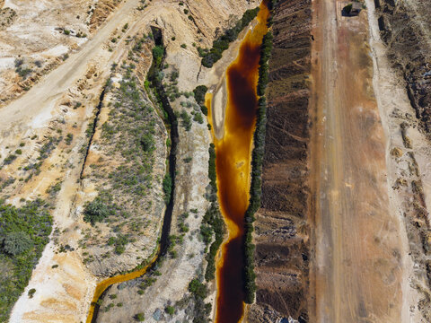 Aerial view of the polluted orange river flowing through the arid landscape of the Achada do Gamo mine site in Achada do Gamo, Beja, Portugal.