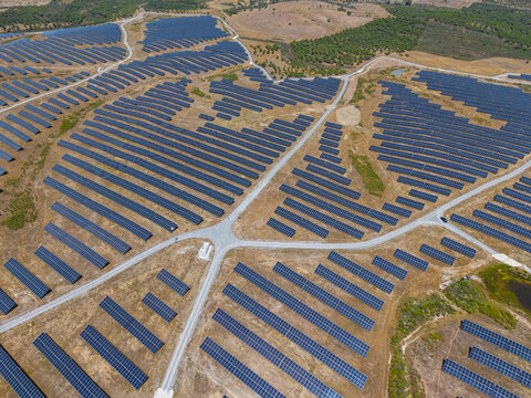 Aerial view of a large solar farm with rows of photovoltaic panels installed on dry, arid terrain, connected by gravel access roads in Gioes, Faro, Portugal.