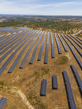 Aerial view of rows of photovoltaic solar panels installed on dry, sun-baked terrain in the rural landscape of Gioes, Faro, Portugal.