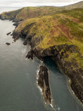 Aerial view of rugged coastal cliffs and a dramatic sea stack rising from the Atlantic Ocean along the green landscape of the coastline in Cork, County Cork, Ireland.