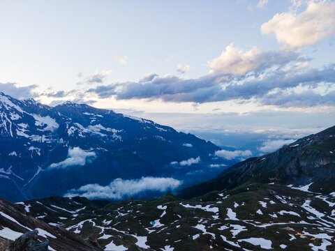 Aerial view of Grossglockner High Alpine Road winding through snow-capped peaks and alpine meadows under a cloudy sky in Zell am See District, Salzburg, Austria.