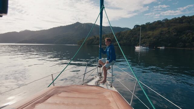 Young man enjoys the morning time on the sailing boat anchored in the calm bay