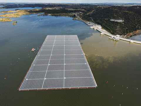 Aerial view of the floating solar farm on the Barragem de Alqueva reservoir with rows of solar panels surrounded by water and hills in Moura, Distrito de Evora, Portugal.