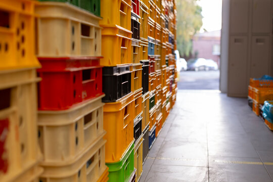 rows of stacked plastic crates in yellow, red, black, green, and beige line warehouse aisle, with shallow depth of field, soft light, and storage order, with crate
