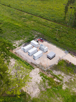 Aerial view of a battery energy storage system with white containers inside a fenced enclosure surrounded by forest in Suntazi, Ogre Municipality, Latvia.