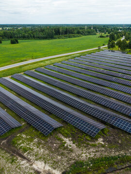 Aerial view of a large solar farm with rows of photovoltaic panels set in a green landscape near a road in Suntazi, Ogre Municipality, Latvia.