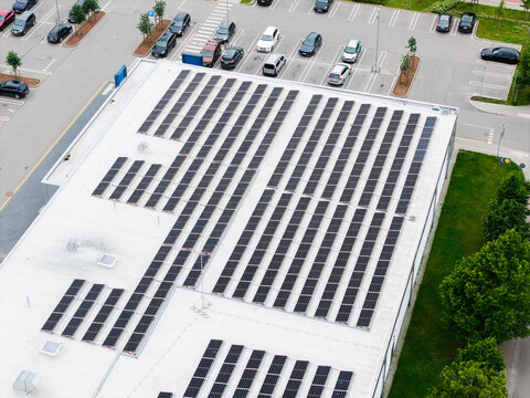 Salaspils, Latvia - 25 June 2026: Aerial view of solar panels installed on the flat roof of a grocery store with a parking lot and surrounding greenery.