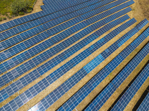 Aerial view of rows of solar panels in a solar farm, set against dry, sun-baked earth in the rural landscape of Vaqueiros, Faro District, Portugal.