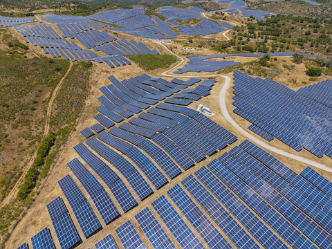 Aerial view of a large solar farm with rows of photovoltaic panels installed on hilly terrain in Vaqueiros, Faro District, Portugal.