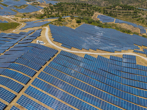 Aerial view of a large solar farm with rows of photovoltaic panels installed on hilly terrain in the rural landscape of Vaqueiros, Faro District, Portugal.