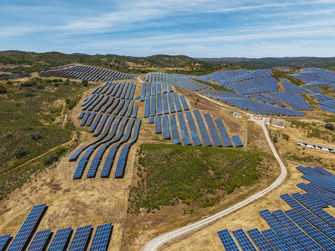 Aerial view of a large solar farm with rows of photovoltaic panels installed on rolling hills in the rural landscape of Vaqueiros, Faro District, Portugal.