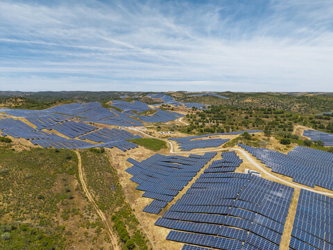 Aerial view of a large solar farm with rows of photovoltaic panels installed across the rolling hills of the countryside in Vaqueiros, Faro District, Portugal.