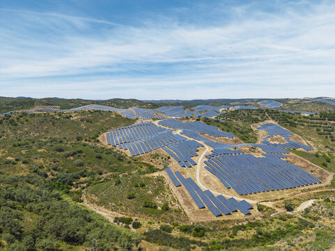 Aerial view of a large solar farm with rows of photovoltaic panels installed on rolling hills in the rural landscape of Vaqueiros, Faro District, Portugal.