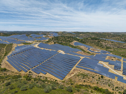 Aerial view of a large solar farm with rows of photovoltaic panels installed on rolling hills in the rural landscape of Vaqueiros, Faro District, Portugal.