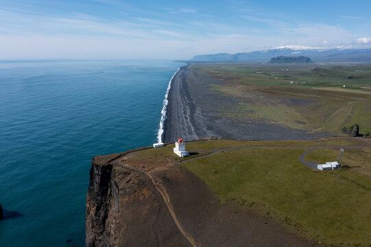 Aerial view of Dyrholaey lighthouse perched on a dramatic cliff overlooking the vast black sand beach and the Atlantic Ocean in Vik, Myrdalshreppur, Iceland.