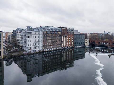 Aerial view of historic and modern buildings along the Spree river with reflections in the water and the Oberbaumbrucke in the background in Berlin, Berlin, Germany.