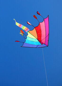 Colorful rainbow kite flying high in clear blue sky on sunny day
