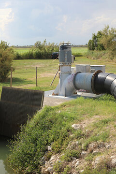 Water pumping station with electric motor and large pipe near an agricultural canal in the countryside