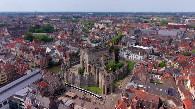 Aerial view video clip of historical Gravensteen medieval castle, city tram, river canal, Flemish gabled houses, and urban cityscape of Ghent in Belgium on a sunny day