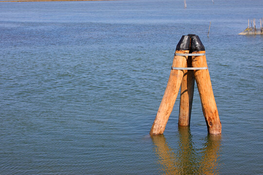 Wooden mooring dolphin pile structure in calm sea water of coastal lagoon