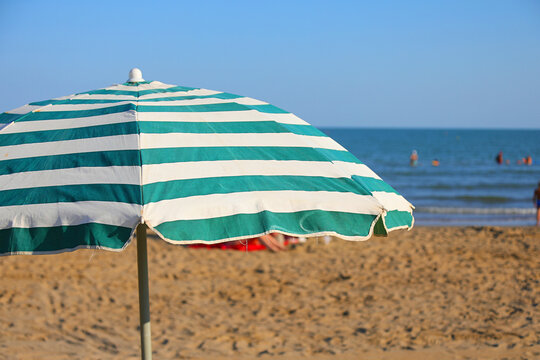 Green and white striped beach umbrella on a sunny sandy shore