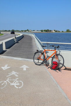 Orange bicycle and red backpack parked along scenic coastal cycle path on sunny day