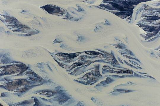 Aerial view of the intricate braided glacial river patterns with white sediment and dark volcanic sand in Vik, Myrdalshreppur, Iceland.