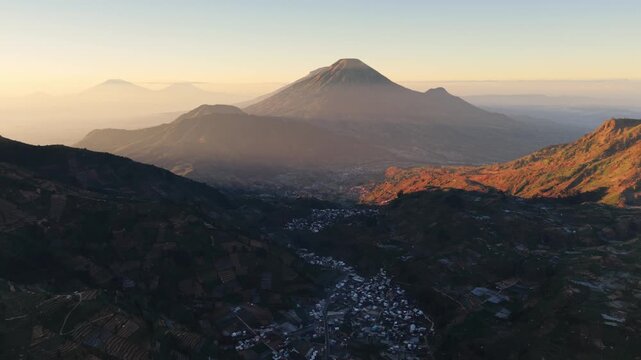Aerial view of volcanic peaks and valley with a small village nestled in the landscape of Indonesia.