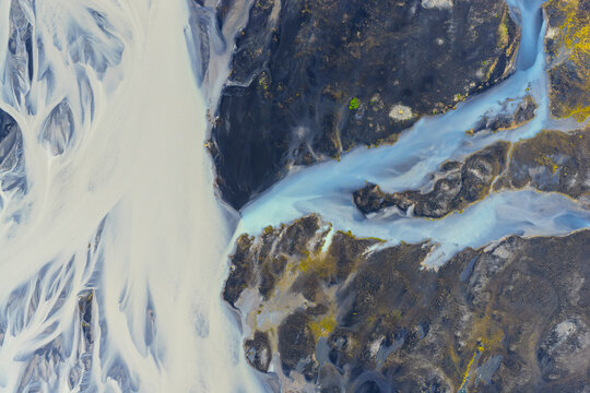 Aerial view of a braided glacial river with sediment-rich water flowing through dark volcanic terrain in Vik, Myrdalshreppur, Iceland.