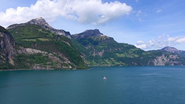 Aerial view of Lake Lucerne with surrounding mountains and lush green slopes under a blue sky in Fluelen, Uri, Switzerland.
