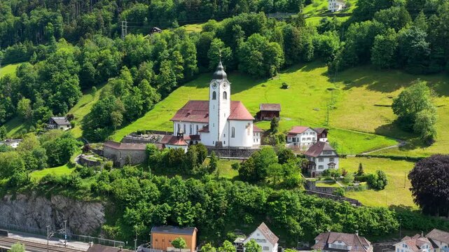 Aerial view of the historic church on a lush green hillside overlooking Lake Lucerne in Fluelen, Uri, Switzerland.