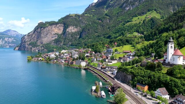 Aerial view of Lake Lucerne and the village of Fluelen with its historic church, railway tracks, and surrounding mountains in Fluelen, Uri, Switzerland.