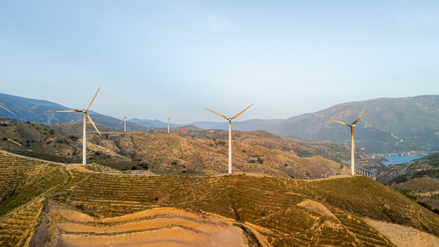 Aerial view of wind turbines situated on arid hills with dry vegetation under a clear blue sky in Velez de Benaudalla, Andalusia, Spain.