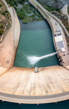 Aerial view of the Presa de Rules dam with water being discharged into the reservoir surrounded by rugged terrain in Granada, Andalucia, Spain.