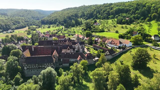 Aerial view of Bebenhausen Monastery, a historic Cistercian abbey with timber-framed buildings and red roofs, surrounded by lush green forests and meadows in Tubingen, Baden-Wurttemberg, Germany.