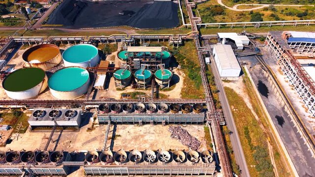 Industrial water treatment tanks and cooling fans. Round liquid storage basins sit near row of cooling fans and metal pipelines at factory.