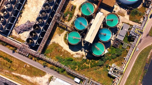 Overhead view of circular water treatment pools and cooling fans. Intricate yellow and metallic pipelines connect round turquoise basins beside mechanical fan units.