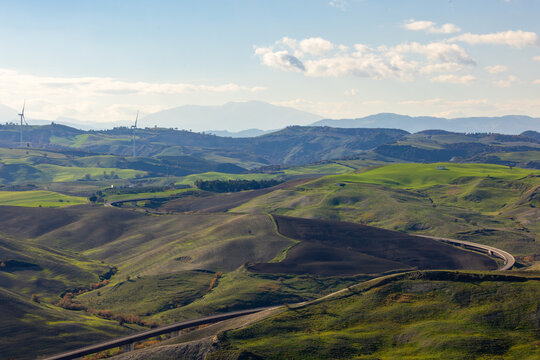 View of rolling green hills, wind turbines, and a winding highway through the landscape in Craco, Basilicata, Italy.
