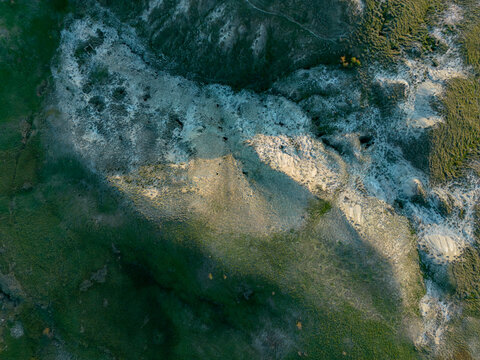 Aerial view of the rugged, eroded landscape and hills surrounding the ghost town of Craco, featuring dramatic light and shadow across the barren terrain in Craco, Basilicata, Italy.