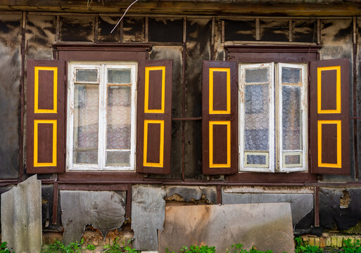 Vilnius, Vilnius County, Lithuania - 09 July 2026: View of the weathered wooden facade and traditional windows with brown and yellow shutters of a historic house in the Snipiskes district.