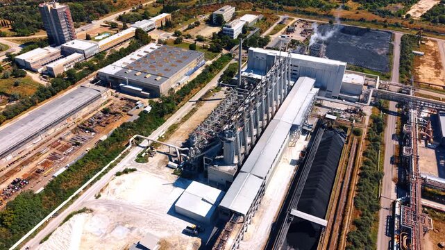 High angle aerial view of a large industrial plant complex. Railway tracks and coal storage piles lay adjacent to steel processing buildings on sunny day.