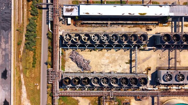 Top down aerial view of industrial cooling system. Direct overhead shot displays two rows of ventilation fans, metal pipes, asphalt road, dirt.