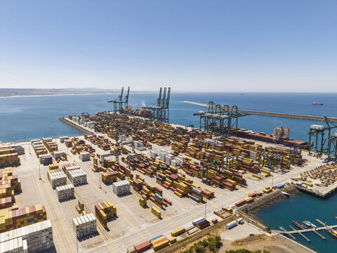 Aerial view of the Port of Sines container terminal with rows of colorful shipping containers, large gantry cranes, and cargo ships docked along the coastline in Sines, Setubal, Portugal.