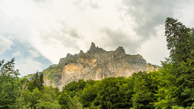View of the dramatic limestone cliffs of the Cirque du Fer a Cheval rising above a dense green forest under a cloudy sky in Sixt-Fer-a-Cheval, Auvergne-Rhone-Alpes, France.
