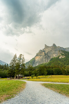 View of the Cirque du Fer a Cheval with its dramatic limestone cliffs, lush green meadows, and a gravel path leading through the landscape in Sixt-Fer-a-Cheval, Auvergne-Rhone-Alpes, France.