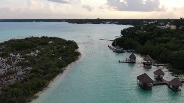 Aerial view of Bacalar Lagoon featuring turquoise water, wooden docks with palapa-roofed structures, and lush vegetation in Bacalar, Quintana Roo, Mexico.