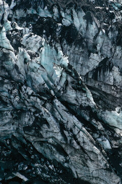 Aerial view of rugged ice formations and deep crevasses of Myrdalsjokull glacier, with contrasts between blue ice and dark volcanic ash in Vik, Myrdalshreppur, Iceland.