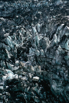 Aerial view of the rugged ice formations and deep crevasses of Myrdalsjokull glacier with dark volcanic ash deposits contrasting against the blue ice in Vik, Myrdalshreppur, Iceland.