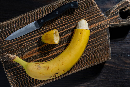 Circumcision concept with cut banana skin and kitchen knife. Conceptual metaphor for male circumcision procedure showing cut yellow banana. Healthcare and medical education photography